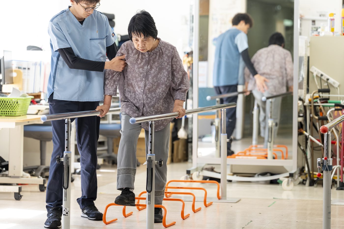 平行棒を使って歩行訓練を行う入所者と、そばで支える理学療法士