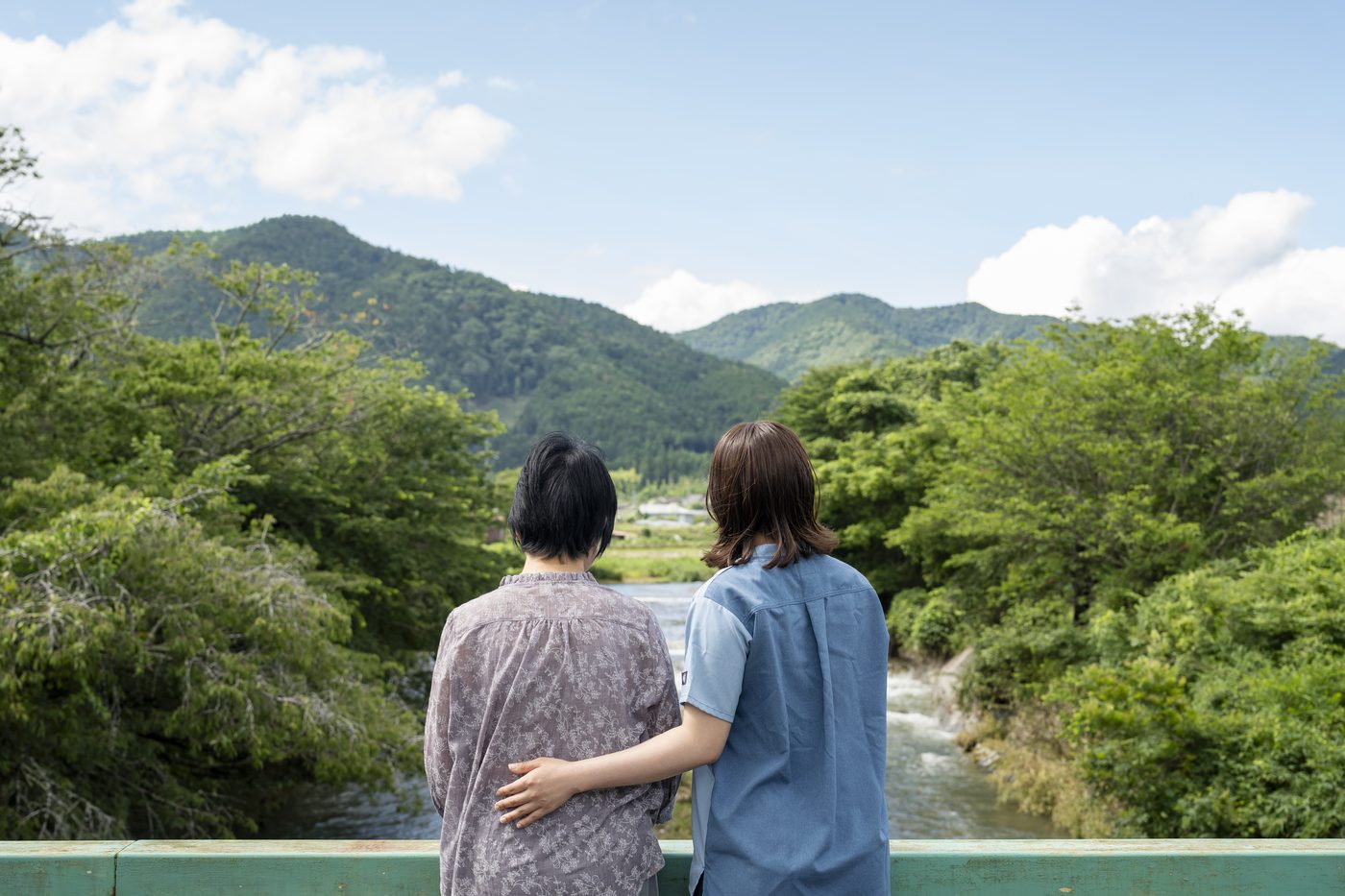 大原の山並みと川を望む橋の上で、寄り添って景色を眺める入所者と職員