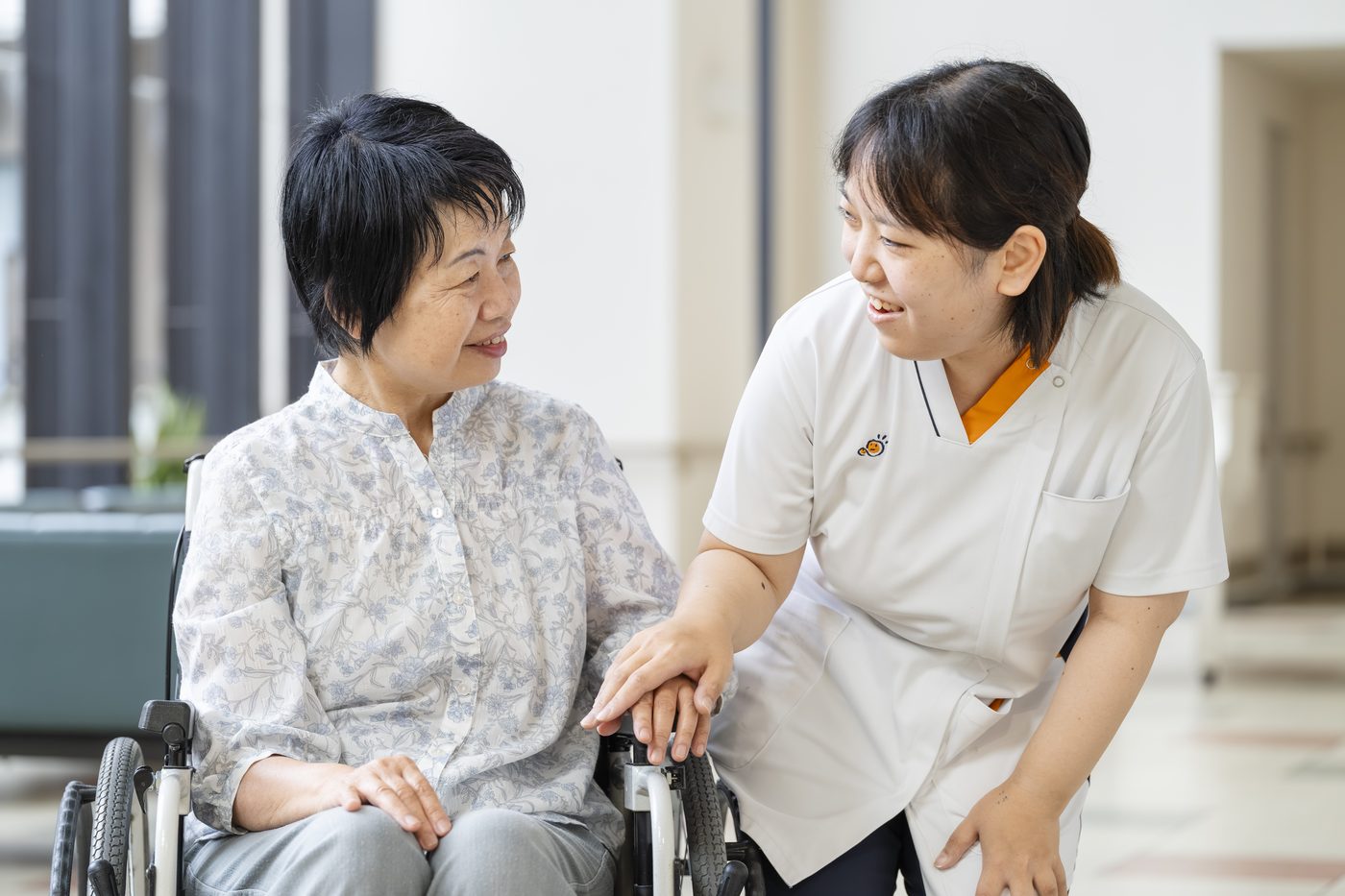 車椅子の入所者にそっと手を添え、笑顔で語りかける介護職員