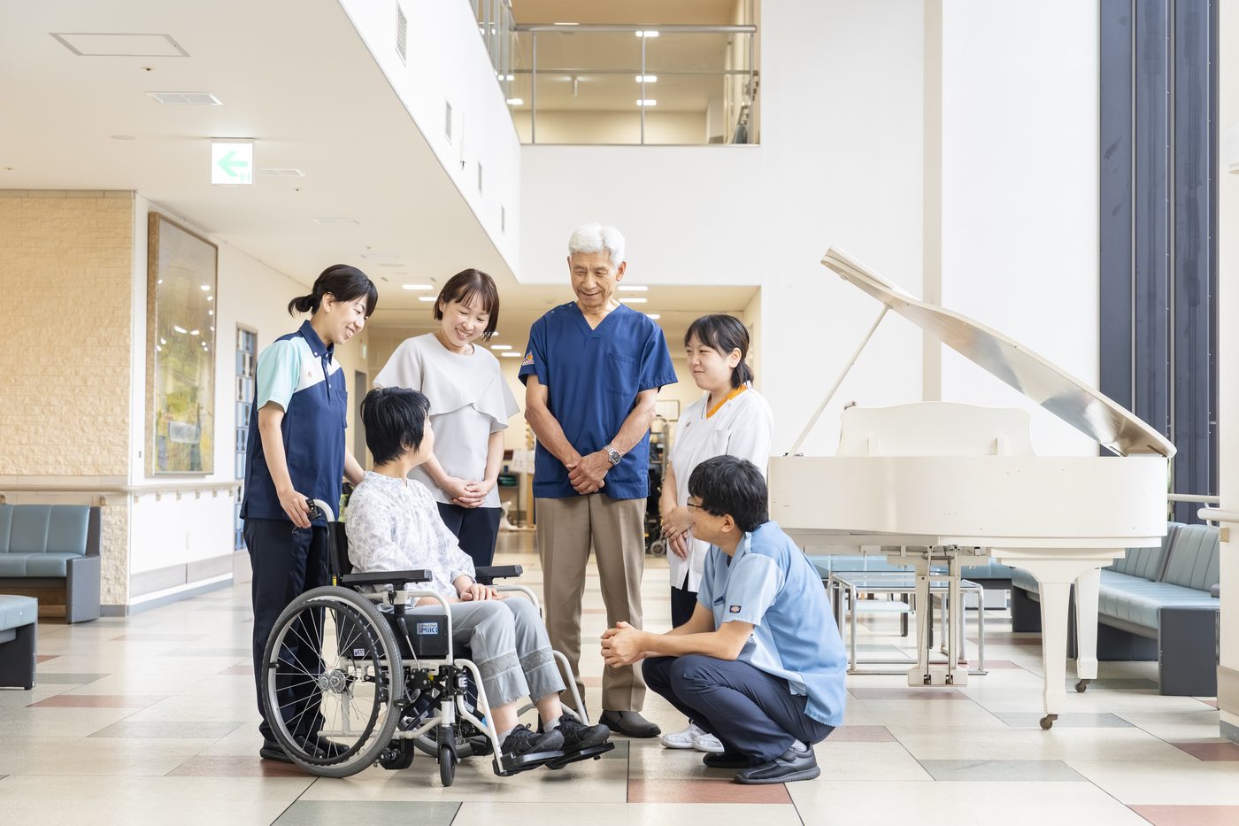 吹き抜けのロビーで、車椅子の入所者とご家族、職員が笑顔で語らう様子